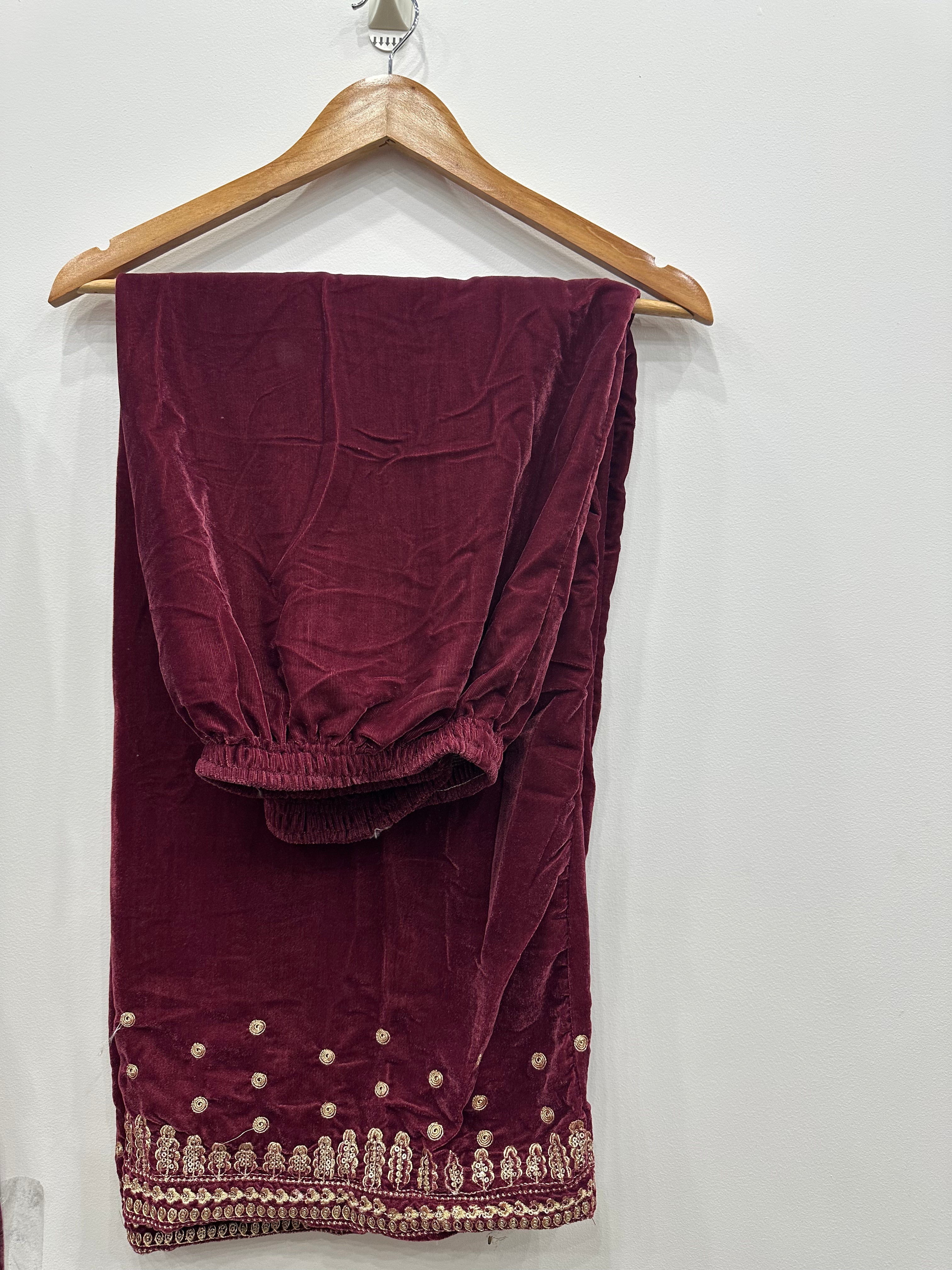 Maroon velvet fabric with gold embroidery on a wooden hanger against a white background
