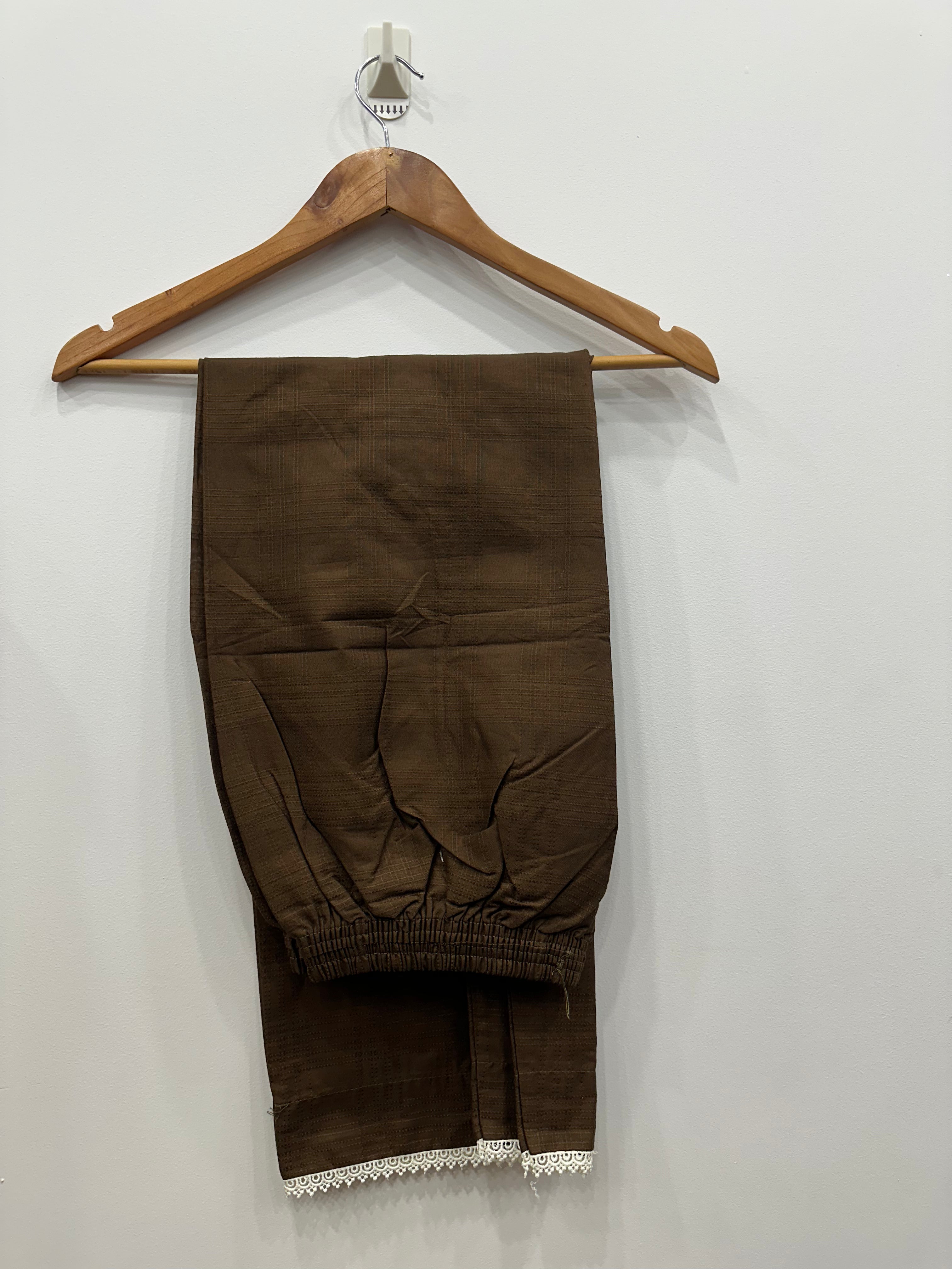 Brown pants with lace trim on a wooden hanger against a white wall