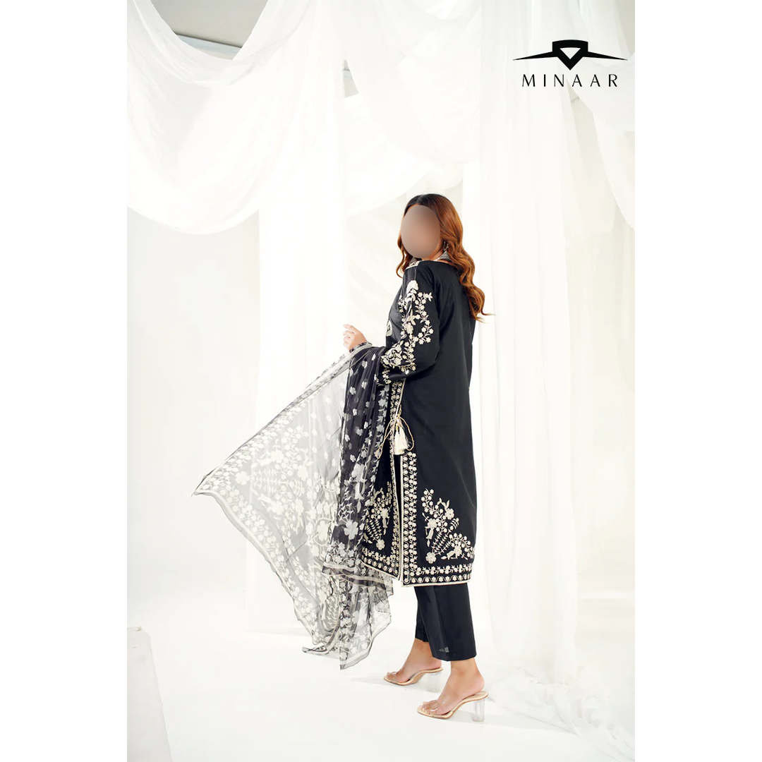 Woman wearing a black embroidered outfit with a sheer overlay, standing against a white background with 'Minaar' branding.