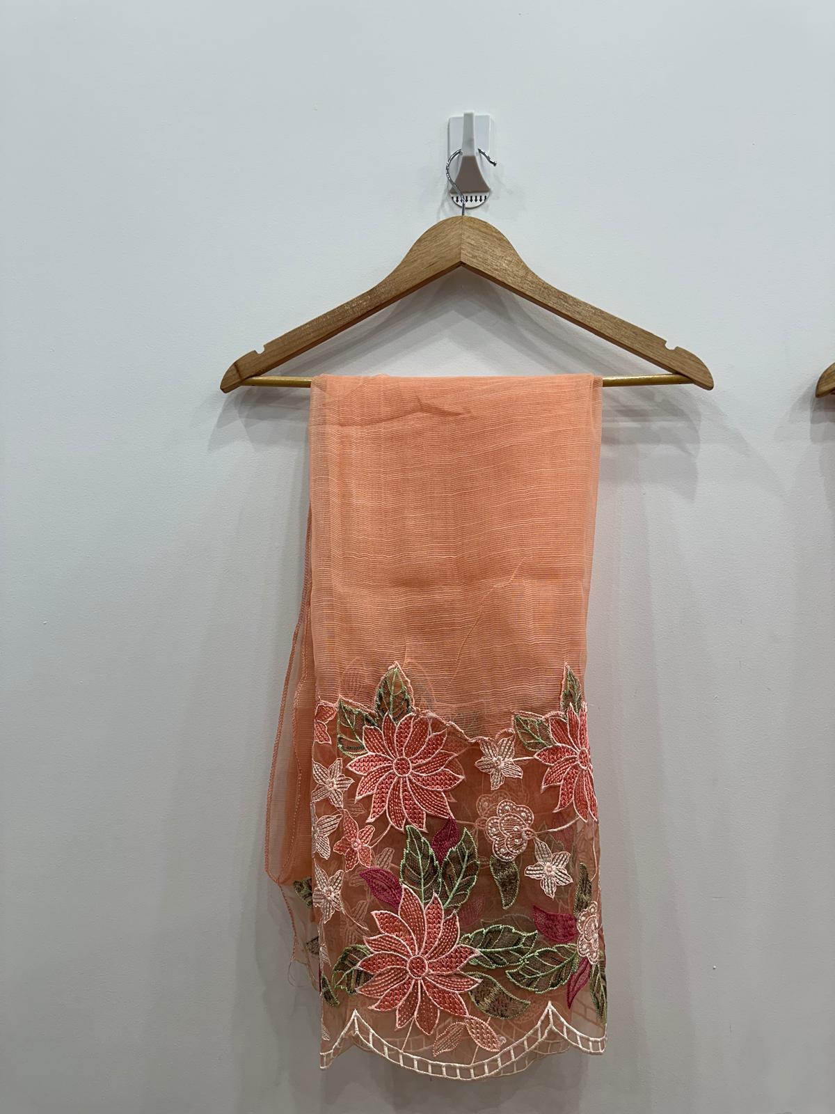 Peach-colored fabric with floral embroidery on a wooden hanger against a white wall.