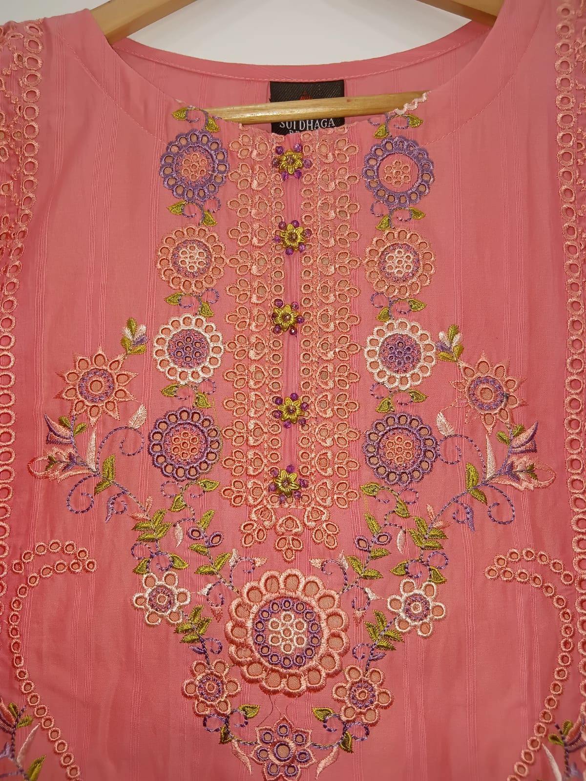 Pink embroidered top with intricate patterns on a hanger