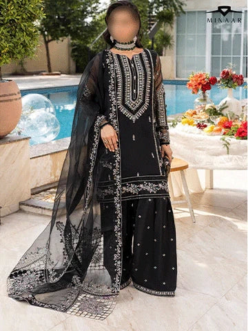 Person wearing a black embroidered outfit with a blurred face, standing outdoors near a pool.