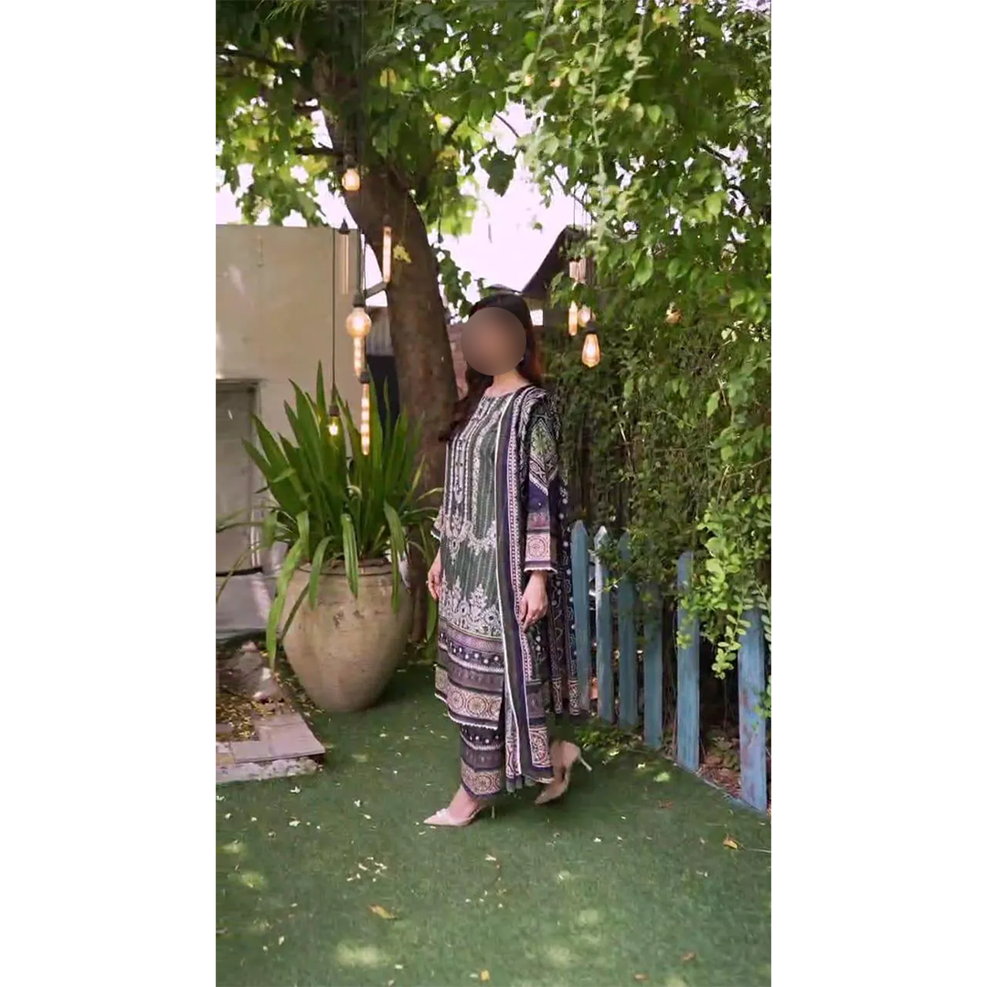 Person wearing a patterned dress standing in a garden with greenery and a building in the background.