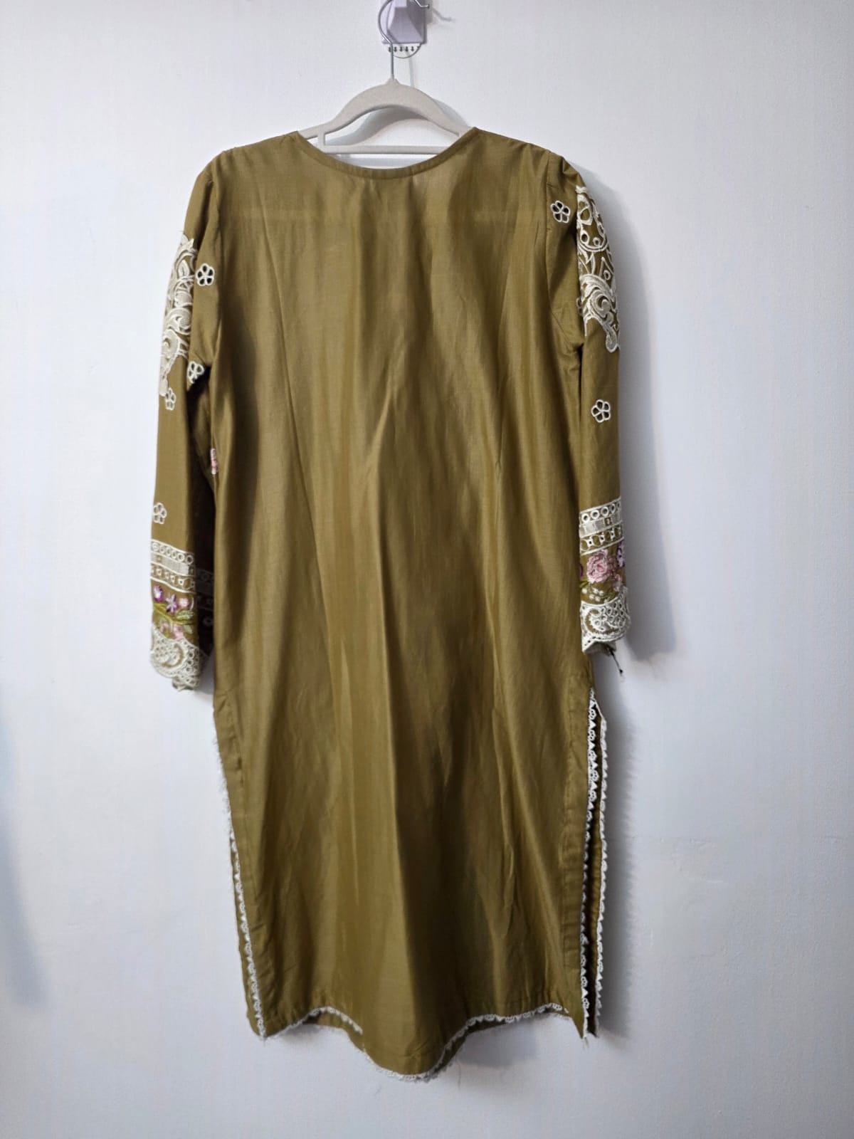 An olive green long-sleeve tunic or kurta with intricate multicolor embroidery on the sleeves and side slits, hanging on a white plastic hanger against a plain light gray wall.