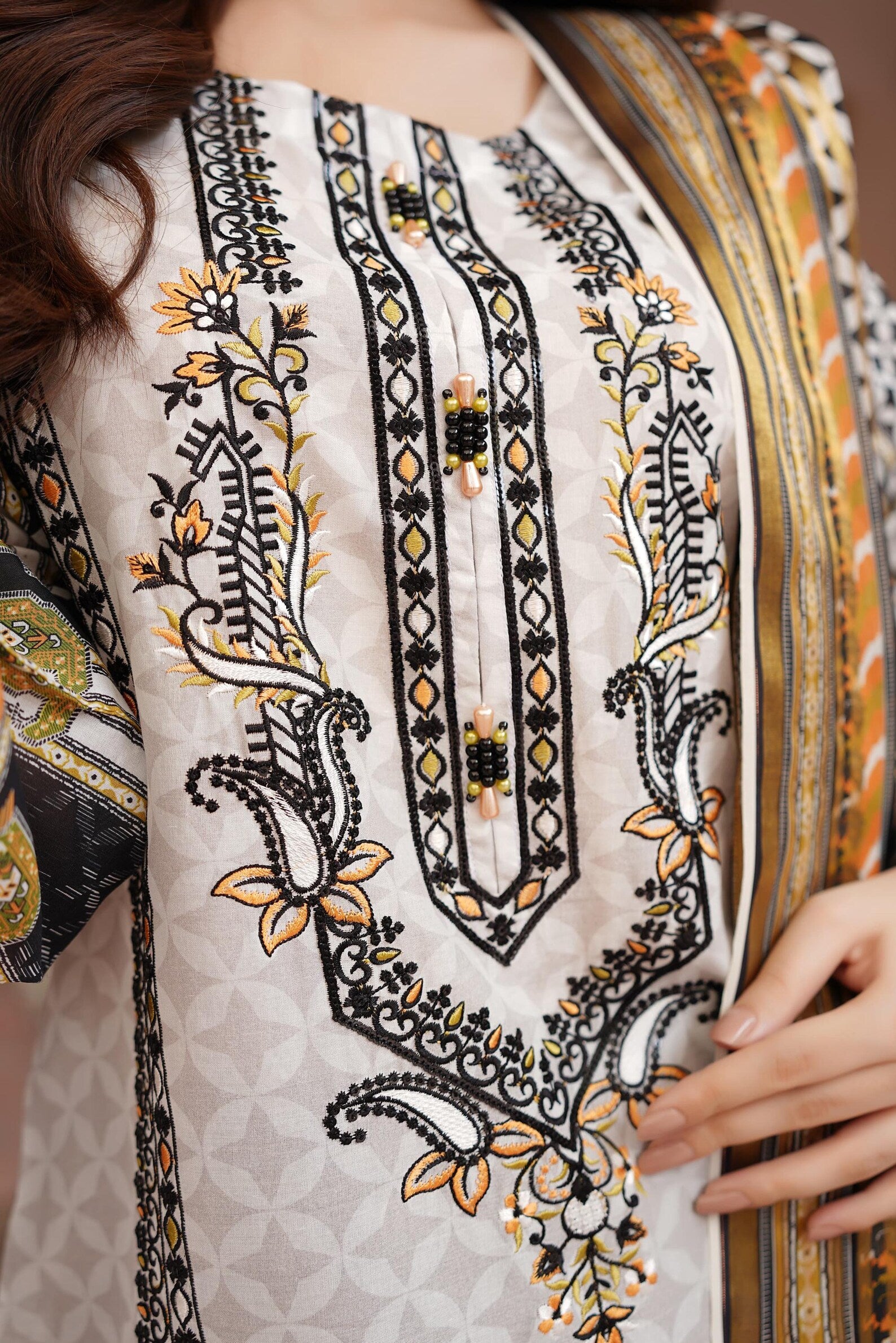 Close-up of a piece of fabric with intricate black and gold embroidery on a white background.